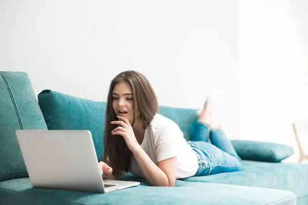 Beautiful young woman watching film on her laptop lying on the sofa — Stock Photo, Image