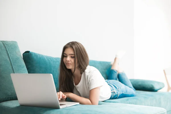 Beautiful young woman watching movie on her laptop lying on the sofa — Stock Photo, Image