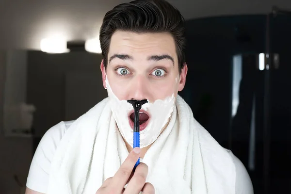 Young handsome man with foam on his face having fun while shaving in bathroom everyday routine — Stock Photo, Image