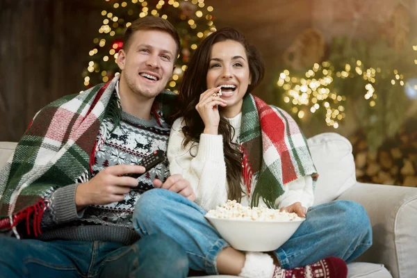 Jeune couple mari et femme enveloppé dans plaid regarder comédie manger pop-corn sur le canapé dans la chambre décorée pour célébrer le Nouvel An humeur festive de Noël — Photo