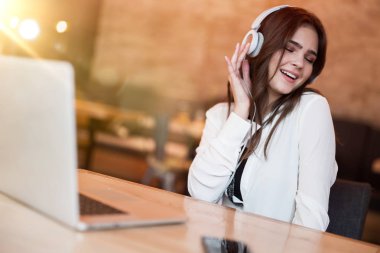 Kulaklıklı genç ve güzel bir kadın en sevdiği müziği laptoptan dinliyor. Öğle yemeğini kafede beklerken kendini özgür hissediyor. Mutlu hafta sonları.