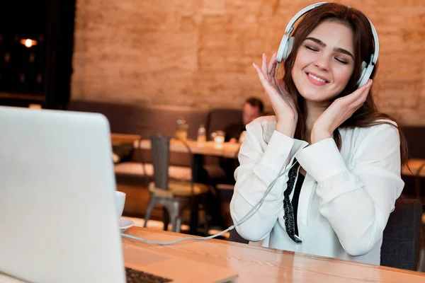 young beautiful woman in headphones listening her favourite music from laptop while waiting her lunch in the cafe happy weekdays