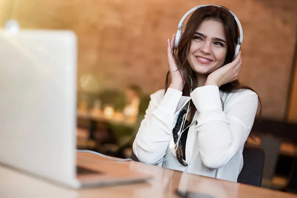 Joven hermosa mujer en los auriculares mirando feliz escuchando su música favorita de la computadora portátil mientras espera su almuerzo en el café alegre semana — Foto de Stock