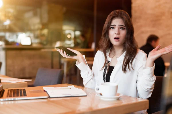 Jong mooi verrast vrouw met telefoon in haar hand werken buiten kantoor in laptop ziet er wanhopig drinken hete koffie in cafe modern zakenvrouw — Stockfoto