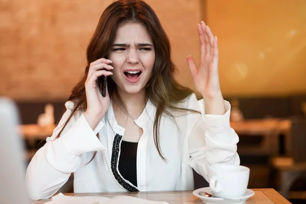 Mujer joven que tiene una conversación telefónica desagradable trabajando fuera de la oficina en su computadora portátil durante la pausa para comer beber café caliente en la cafetería mirando enojada mujer de negocios moderna — Foto de Stock