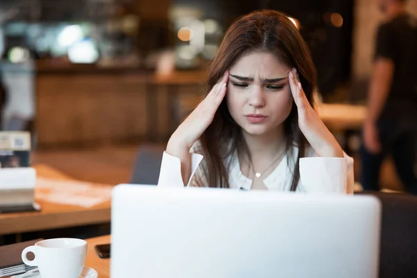 Joven hermosa mujer en chaqueta blanca con estilo de trabajo en su ordenador portátil sensación de depresión después de la jornada laboral estresante sentado en la cafetería de moda moderna mujer de negocios multitarea — Foto de Stock