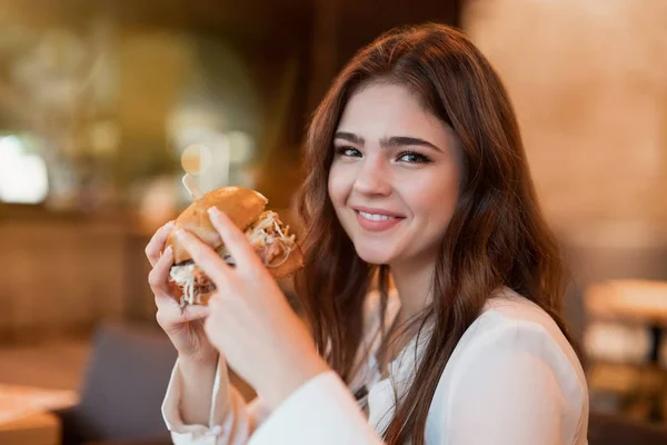 Jong mooi vrouw in wit stijlvol blouse eten vlees hamburger voor lunch in trendy cafe op zoek gelukkig eten buiten — Stockfoto