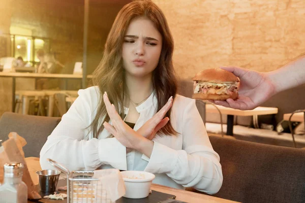 Genç ve güzel bir kadın, elinde taze et burgeriyle garsona bir işaret göstermez. Kafede öğle yemeği sırasında. Düzgün beslenme ve diyete bağlı kalır. — Stok fotoğraf