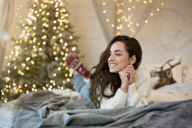 Yeni yılı kutlamak için dekore edilmiş bir odada Noel süveteri ve çorap giyen genç ve güzel bir kadın heyecanlı görünüyor.