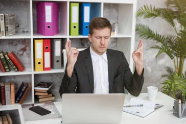 Genç ve yakışıklı yönetici, ofisteki iş yerinde başarılı bir görüşme umuduyla parmaklarını çaprazlayarak oturuyor. Çoklu görev, çalışma konsepti