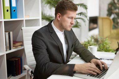 handsome young man in business suit working in his laptop at his working place in office looking concentrated. multitasking, work concept
