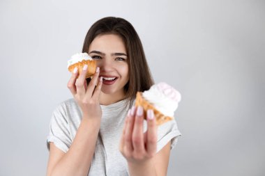 Genç ve güzel bir kadın, elinde kremalı iki tatlı kek tutarken başka bir mutlu, soyutlanmış beyaz arka planda sağlıklı bir hayat sürüyor.