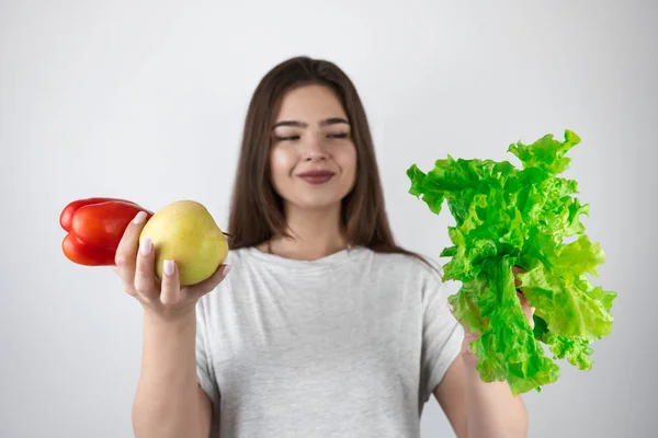 Jovem mulher morena ajuste com salada verde em uma mão e maçã fresca e pimenta vermelha em outro olhar feliz isolado fundo branco estilo de vida vegeterian — Fotografia de Stock