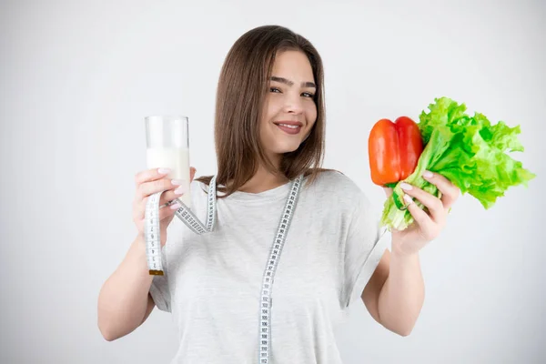 Ung leende kvinna med centimeter runt halsen håller glas kefir och röd paprika med färsk sallad isolerad vit bakgrund dietologi och näring — Stockfoto