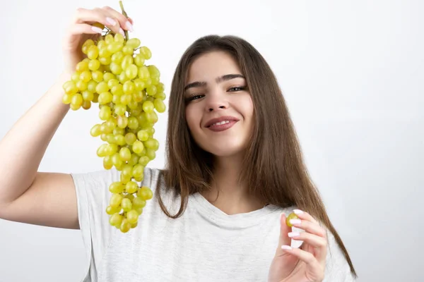Młoda piękna uśmiechnięta kobieta trzyma kilka zielonych winogron stojących na odizolowanym białym tle dietologii i odżywiania — Zdjęcie stockowe