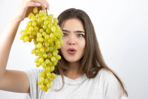 Młoda piękna zaskoczona kobieta stojąca z gronem zielonych winogron stojących na izolowanym białym tle dietologii i odżywiania — Zdjęcie stockowe