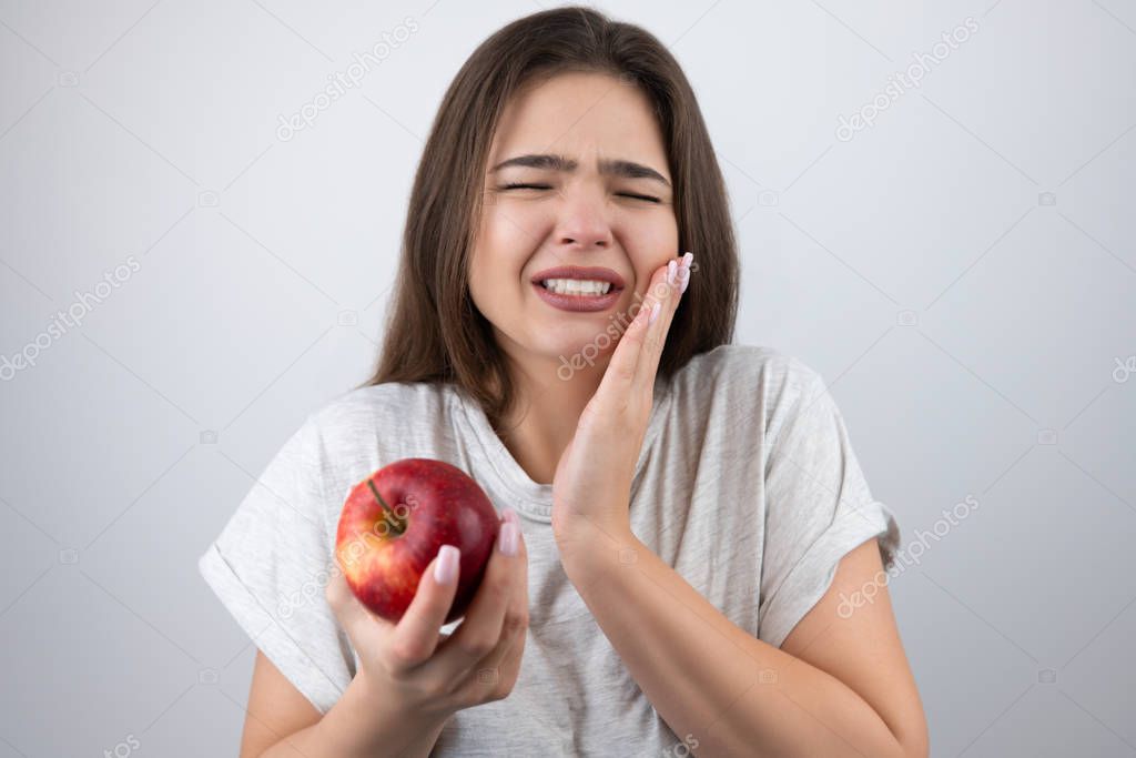 young brunette woman suffering toothache holding red apple in her hand standing on isolated white background healthcare