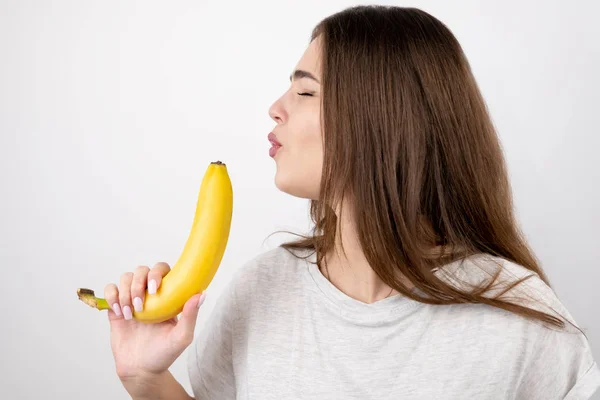 Młoda atrakcyjna kobieta trzymająca banana jak pistolet w ręku wyglądająca zdecydowanie stojąco na białym tle dietetyki i odżywiania — Zdjęcie stockowe