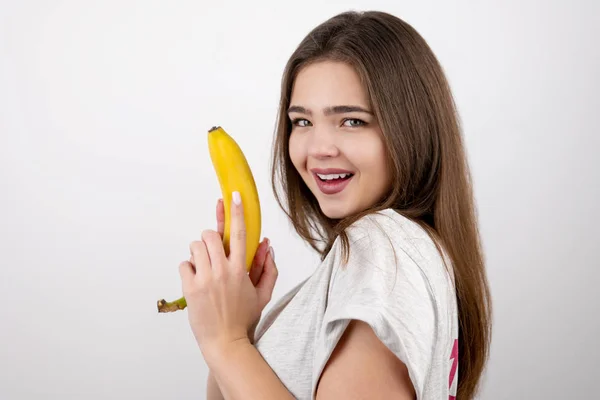 Jovem mulher atraente segurando banana como uma arma na mão olhando sexy em pé no fundo branco isolado dietologia e nutrição — Fotografia de Stock