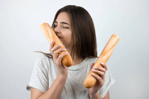 Wanita muda yang menarik mencium setengah baguette di tangannya berdiri di atas dietologi dan nutrisi latar belakang kulit putih yang terisolasi — Stok Foto