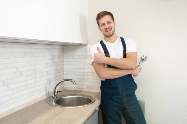 Joven sonriente fontanero en uniforme de pie feliz después de ir buen trabajo en la fijación del fregadero en la cocina que muestra como signo de servicio de reparación profesional — Foto de Stock
