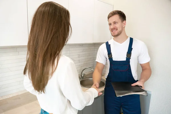young man plumber and brunette woman client shaking hands after successful work on water tap installation professional repair service