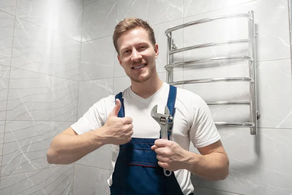 Sonriente hombre trabajador en uniforme con llave en la mano muestra como signo se ve feliz después de hacer exitoso servicio de reparación profesional — Foto de Stock