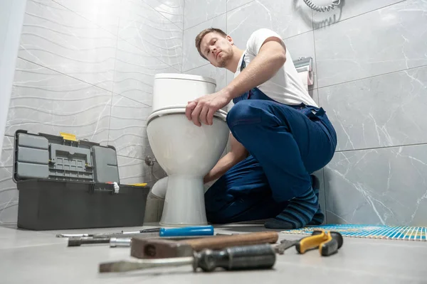 Hombre fontanero en uniforme reparación inodoro utilizando kit de instrumentos servicio de reparación profesional — Foto de Stock