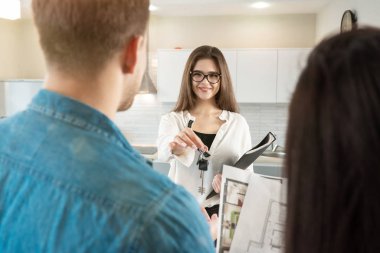 Kadın emlak satış müdürü, başarılı bir emlak anlaşmasından sonra mutlu müşterilere anahtar veriyor.