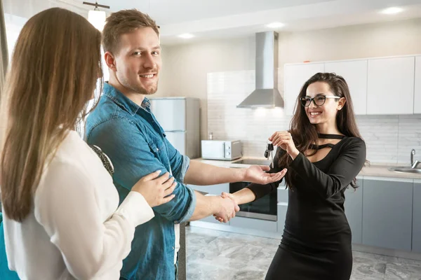 brunette woman realtor property manager giving keys to lovely satisfied clients couple man and woman shaking hands at cosy appartments after successful lease sign