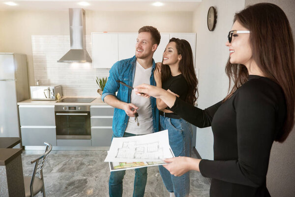 attractive woman realtor property manager showing new appartment for rent to young beautiful couple husband and wife