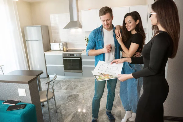 attractive woman realtor property manager showing plannings of new appartment on sale to young beautiful couple husband and wife