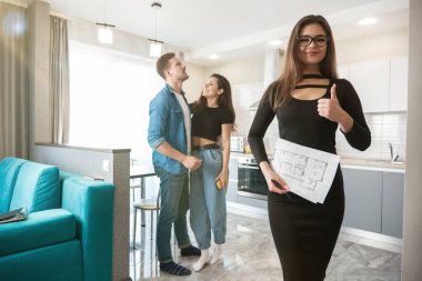 Çekici kadın emlakçı emlakçı genç karı ve kocayla emlak anlaşmasında başarılı bir iş birliği yaptıktan sonra tabela gibi görünüyor.