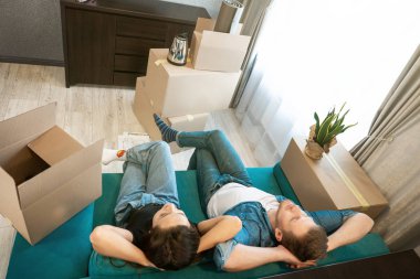 Genç bir çift, yeni apartman dairesine taşınırken kanepede mola verirken yorgun görünüyorlar.