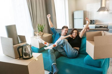 Genç bir çift, yeni apartman dairelerine taşınırken koltukta ellerini havaya kaldırarak mola verirken mutlu görünüyorlar.