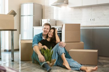 Genç çift, yeni apartman dairelerine taşınırken mutfak zemininde otururken mutlu görünüyorlar.