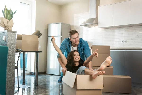 Young couple man and woman having fun while unpacking boxes and moving in new appartment. husband carrying his wife in box on the floor — Stock Photo, Image