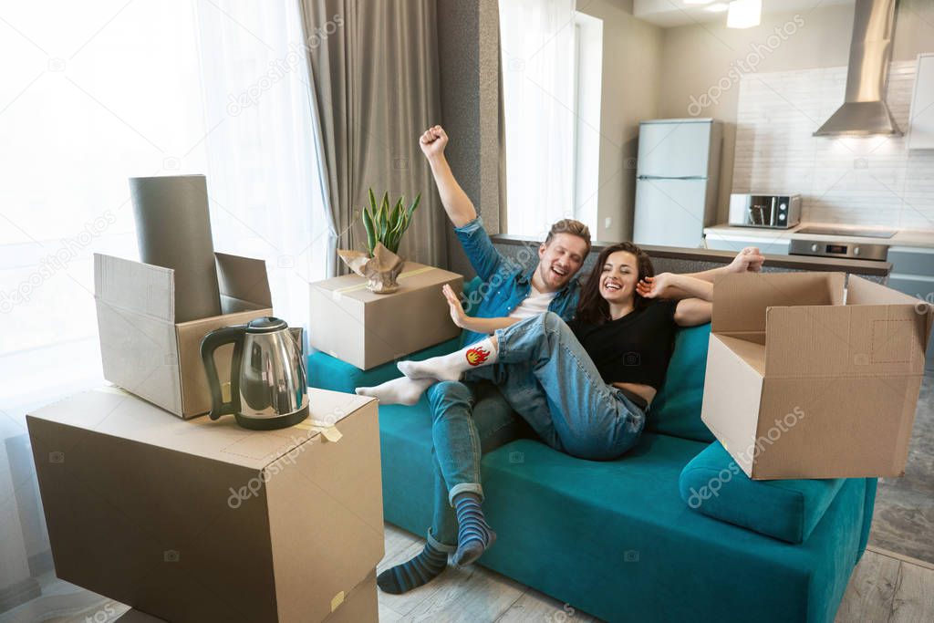 young couple man and woman looking happy having break on the sofa during moving to new appartment unpacking boxes