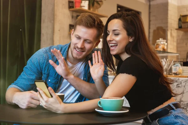 Νεαρό ζευγάρι όμορφη γυναίκα και όμορφος άντρας που έχουν σε απευθείας σύνδεση συνομιλία με τους φίλους στο καφέ πίνοντας ζεστό καφέ αναζητούν χαρούμενος — Φωτογραφία Αρχείου