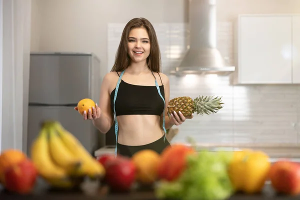 Mladá fit žena s centimetrem kulatý krk nosí černý top a kamaše drží ananas v jedné ruce a pomeranč v jiné dietologii a výživy — Stock fotografie