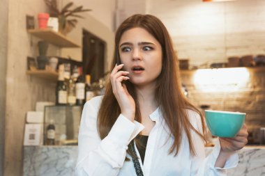 Genç, güzel esmer kadın kafede sıcak kahve içerken telefonla konuşuyor. Şaşırmış görünüyor.