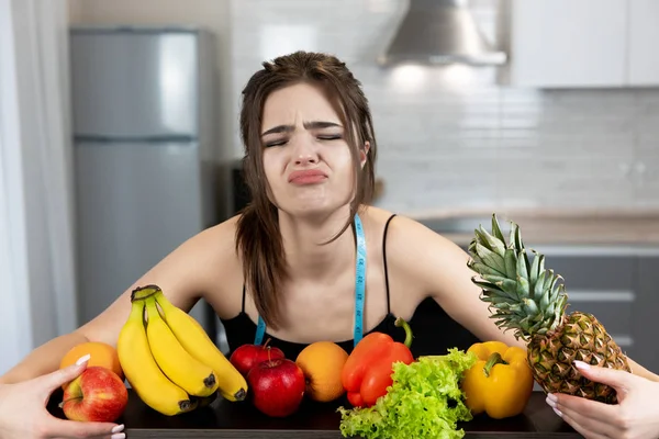 Jovem mulher apto com centímetro de pescoço redondo vestindo top de esportes preto em pé na cozinha cheia de frutas parece chateado dietologia e nutrição — Fotografia de Stock