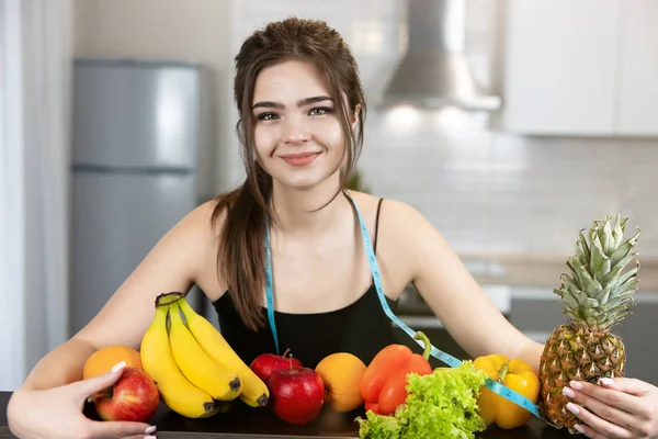 Jovem mulher apto com centímetro de pescoço redondo vestindo top de esportes preto em pé na cozinha cheia de frutas parece feliz e satisfeito dietologia e nutrição — Fotografia de Stock