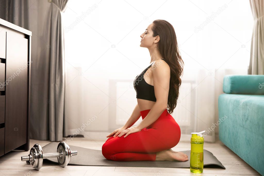 sexy fit beautiful woman in sportwear doing everyday warm up exercises with dumbbell on the floor at home, healthy lifestyle