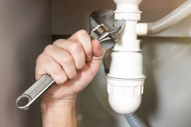 Adamın eli ayarlanabilir anahtarı lavabo borusunun yanında tutuyor. Profesyonel tesisat onarım servisi.