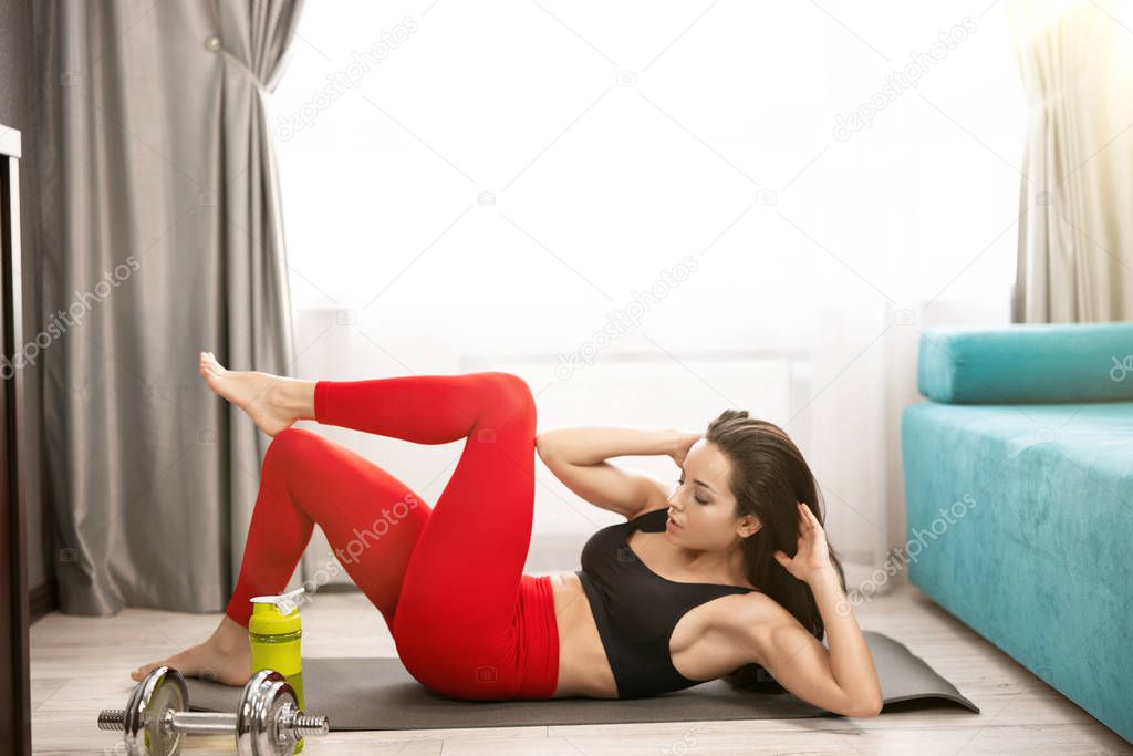 young fit brunette woman in sportwear doing abdominals with crunch and leg up on the mat in living room during home workout, sportive lifestyle