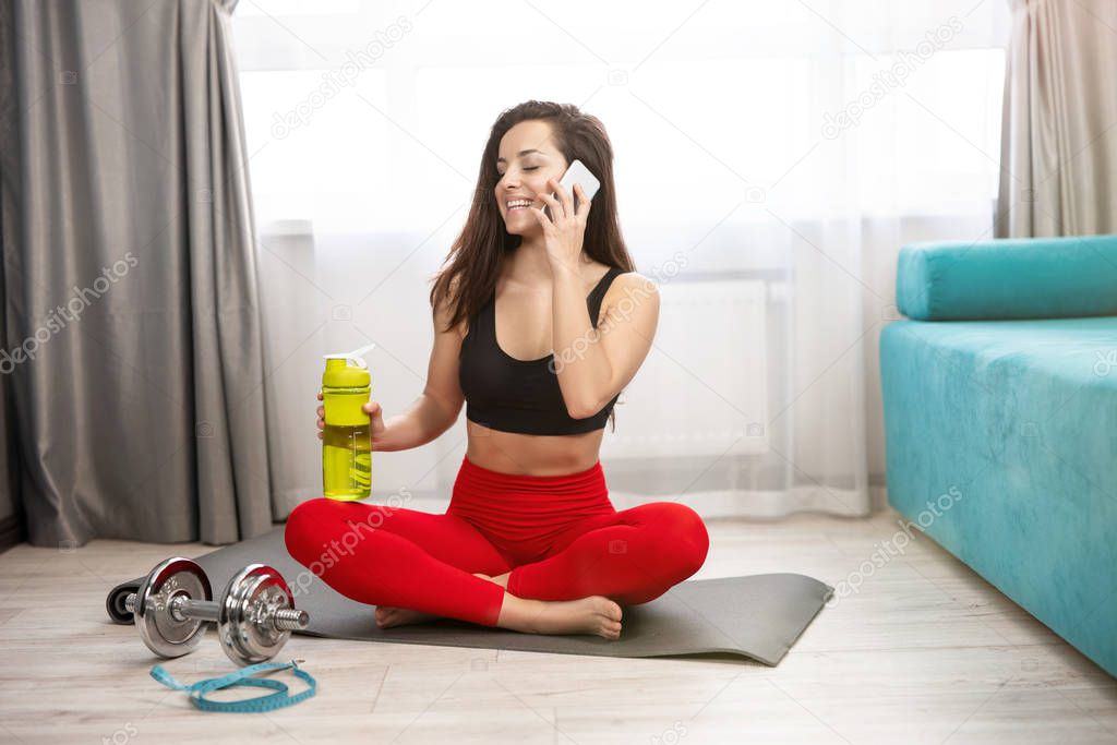young fit beautiful woman in sportwear talking on her smartphone during daily home workout on the mat in living room, sportive lifestyle