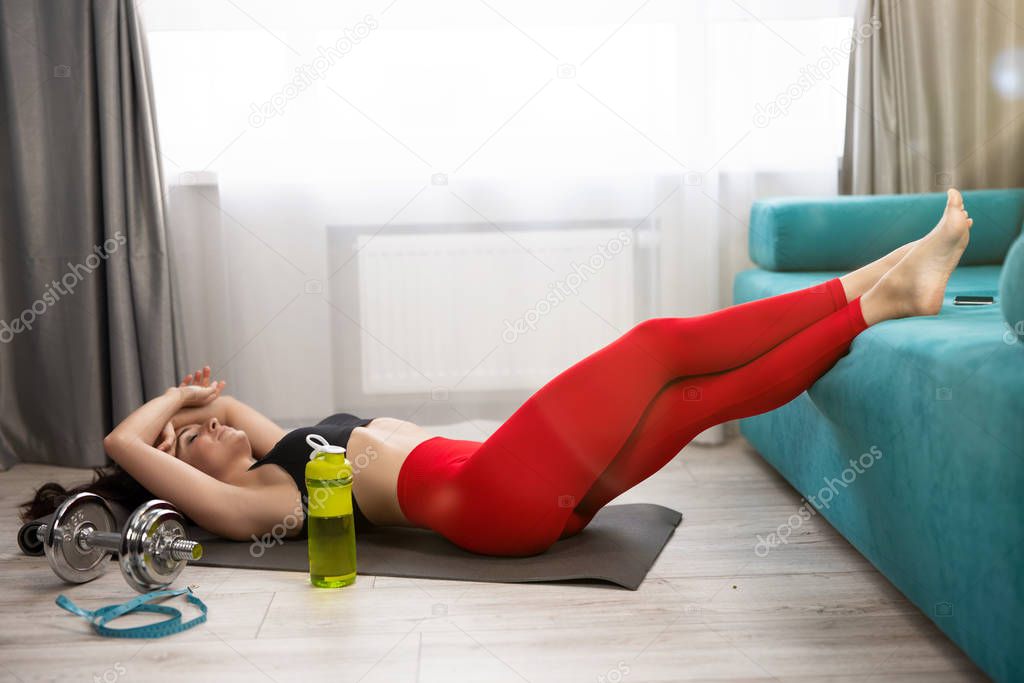 young fit beautiful woman in sportwear lies on the floor looking tired after daily home workout on the mat in living room, sportive lifestyle