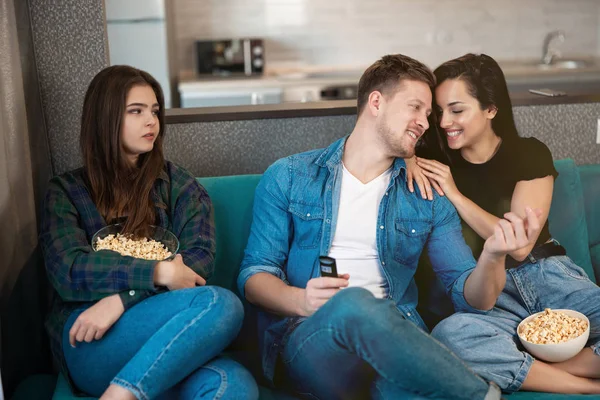 Jeune fille jalouse regardant le couple frémissant assis ensemble sur le canapé intérieur. Concept d'amitié, de jalousie et de triangles d'amour — Photo