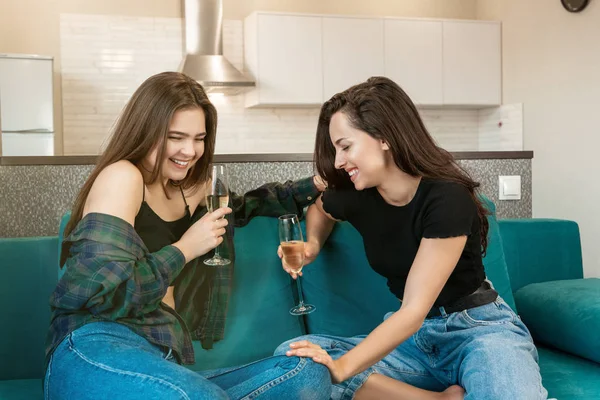 Due giovani belle amiche che bevono champagne sul divano ridendo e divertendosi, festeggiando l'amicizia — Foto Stock